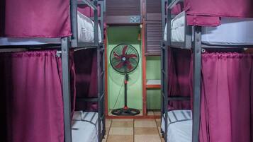 Un dormitorio con literas, un ventilador de pie y una pared verde.