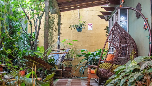 A narrow, tiled corridor with hanging plants and a wicker chair. -  Gardens House, Airport Juan Santamaría, Alajuela, San Jose (Alajuela)