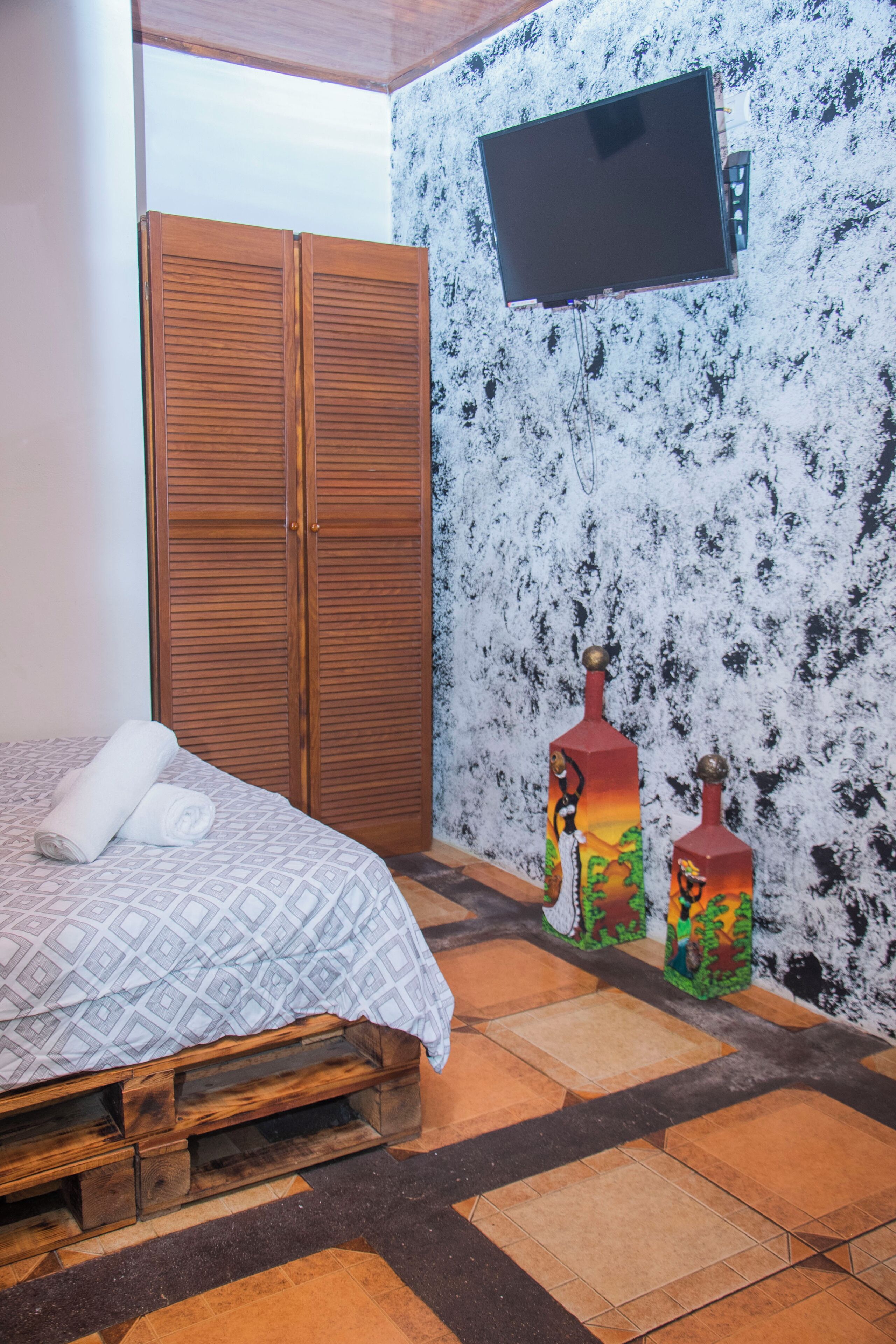 A bedroom with a wooden bed, a TV mounted on the wall, and two decorative bottles.