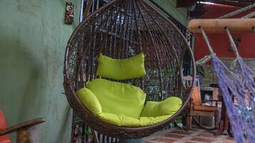 A wicker hanging chair with bright green cushions in a room with tiled flooring and a wooden ceiling.
