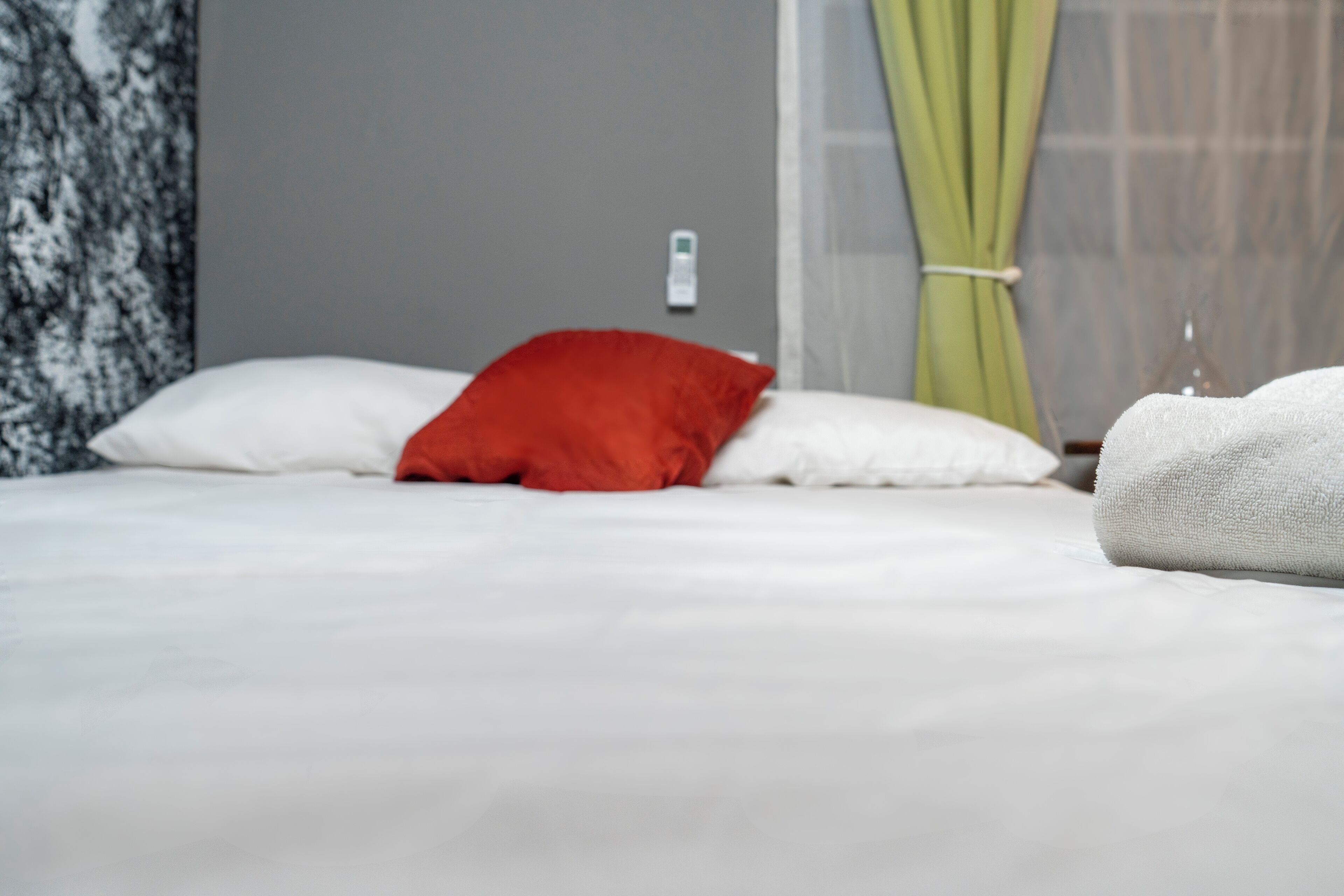 Una cama con almohadas blancas y rojas, una toalla blanca y una cortina verde.
