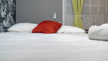 Una cama con almohadas blancas y rojas, una toalla blanca y una cortina verde.