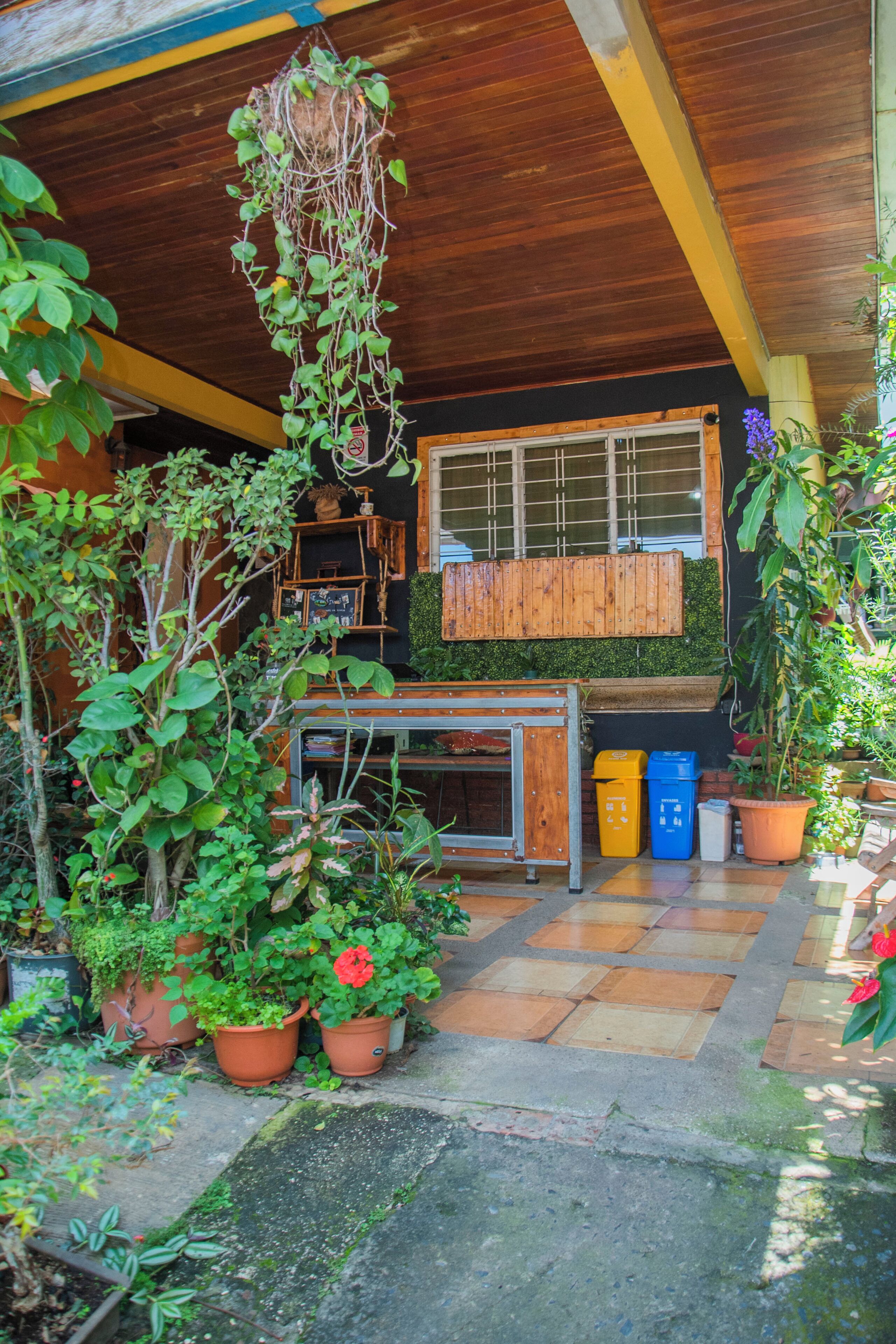 A covered outdoor area with wooden beams, potted plants, and a tiled floor.