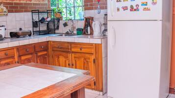 Una cocina con armarios de madera, un refrigerador blanco y una mesa de madera con un taburete.