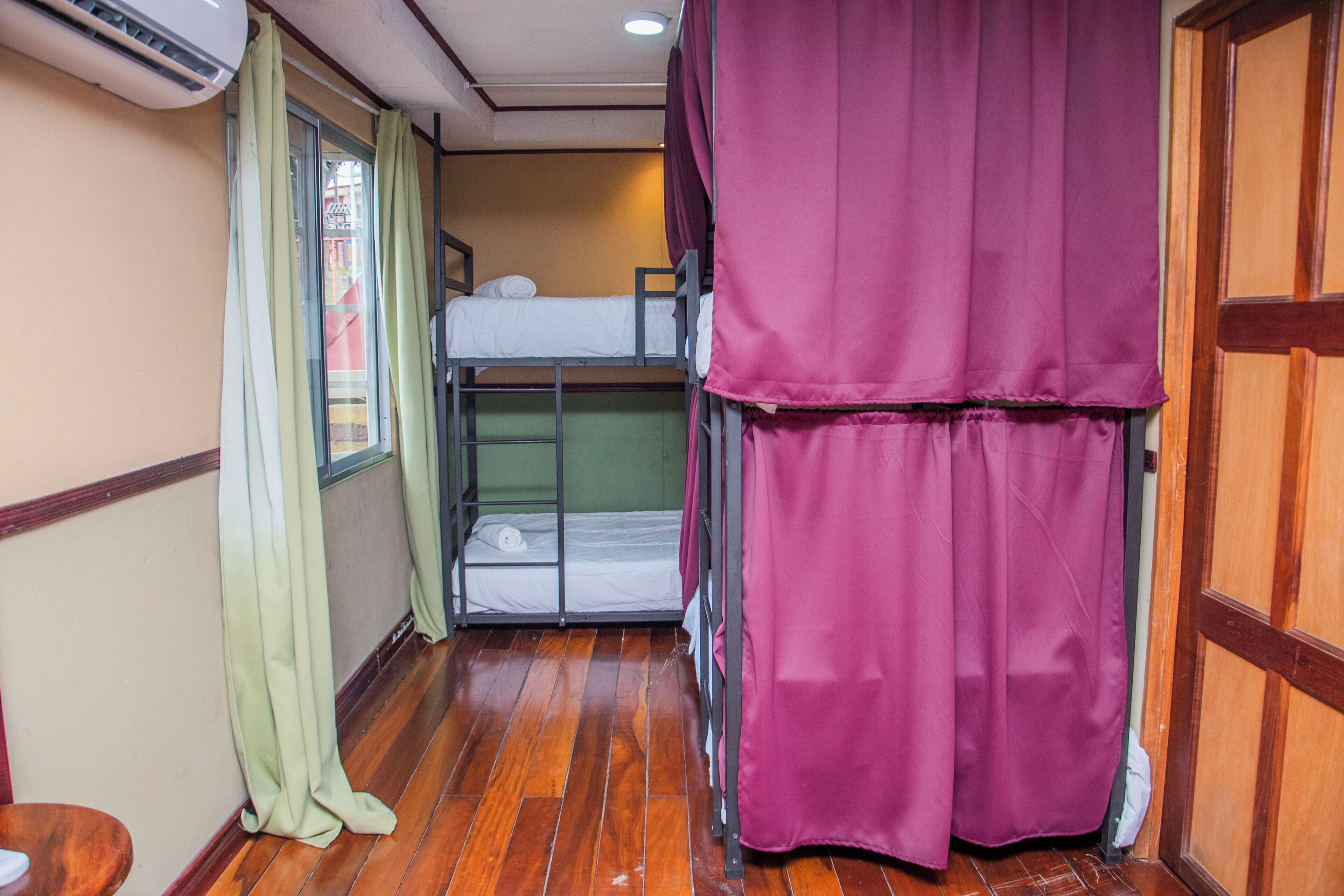 A bunk bed room with a wooden floor, a window with curtains, and a door.