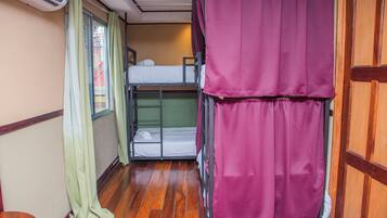 Habitación con literas, piso de madera, ventana con cortinas y una puerta.