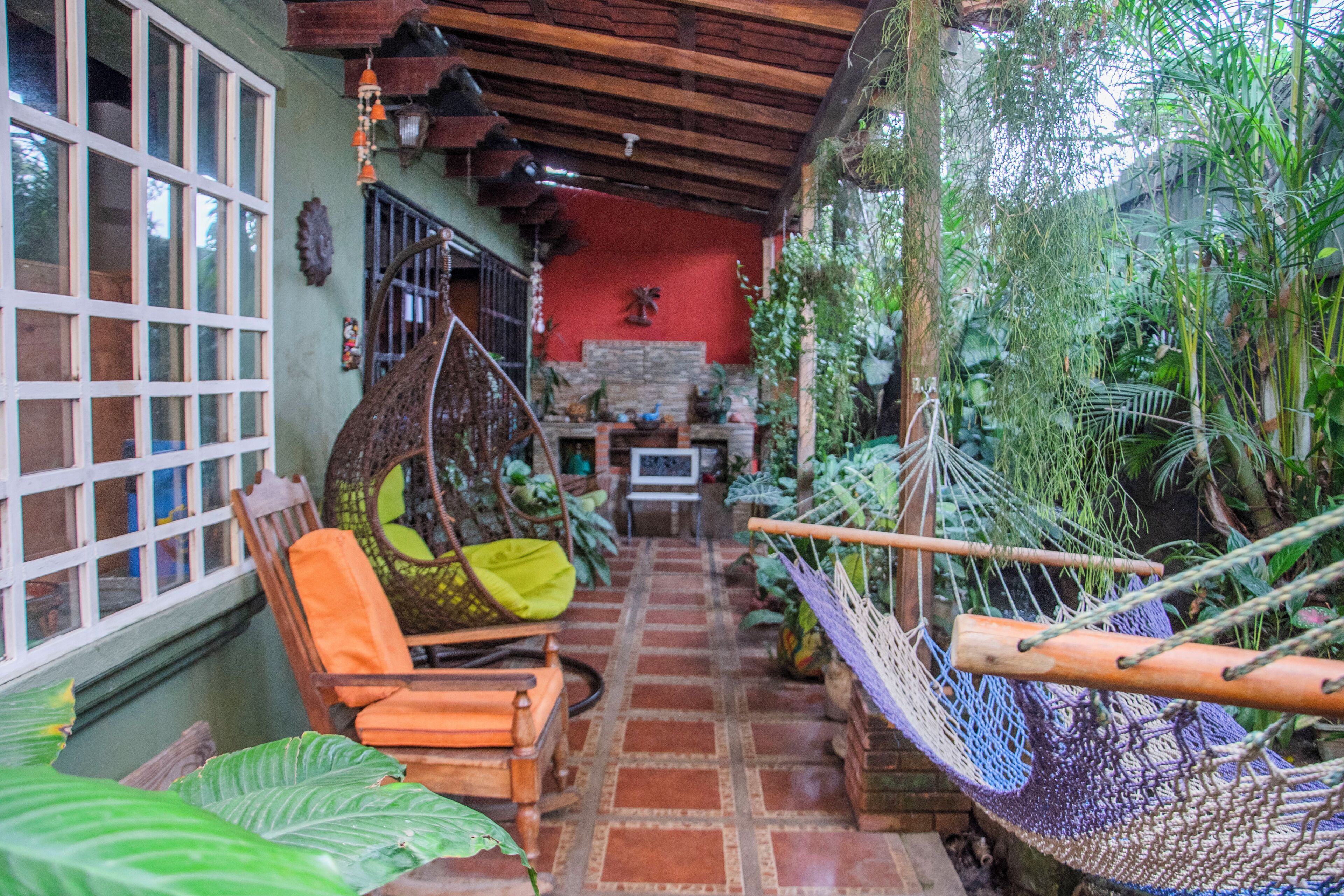A cozy room with a hammock, a wooden chair with cushions, a tiled floor, and a red wall with a decorative item.