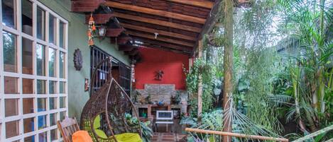 A cozy room with a hammock, a wooden chair with cushions, a tiled floor, and a red wall with a decorative item.