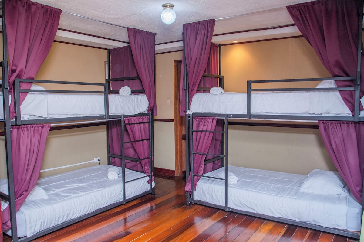 A room with bunk beds, purple curtains, and wooden flooring.