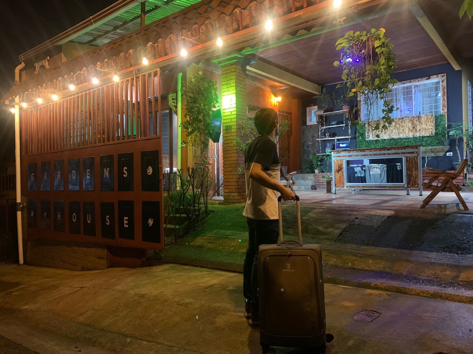 A person with a suitcase at a hotel entrance with a sign reading "GARDEN HOUSE".