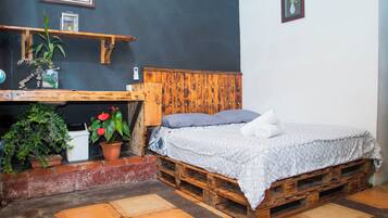 Une chambre à coucher au style rustique, avec un lit en bois, une petite table ornée de plantes et un mur sombre décoré de tableaux encadrés.