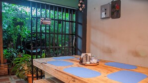 A wooden table with blue placemats, a bench, and a view of lush greenery through a barred window. -  Gardens House, Airport Juan Santamaría, Alajuela, San Jose (Alajuela)