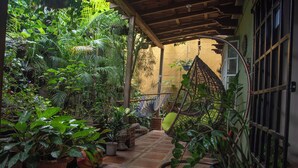 A covered patio area with a hammock, potted plants, and a tiled floor. -  Gardens House, Airport Juan Santamaría, Alajuela, San Jose (Alajuela)