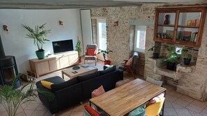 A cozy living room with a sofa, TV, fireplace, and a dining area with chairs and a table. - Gite de Charme Rénové Dans le Lot (Douelle)