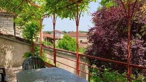 A wooden deck with a table and chairs, surrounded by greenery and a red metal pergola. - Gite de Charme Rénové Dans le Lot (Douelle)