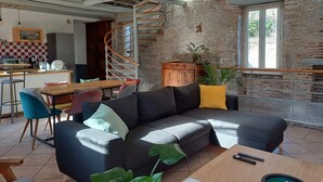 A cozy living room with a modern sofa, a wooden coffee table, and a spiral staircase leading to an upper level. - Gite de Charme Rénové Dans le Lot (Douelle)