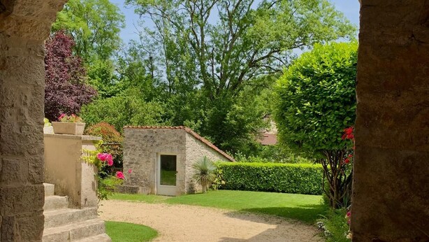 A stone archway leading to a small stone building with a door, surrounded by a well-maintained garden and trees. - Gite de Charme Rénové Dans le Lot (Douelle)