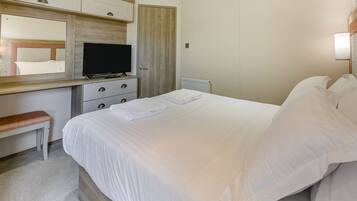 A hotel room with a bed, a desk with a television, a bench, and a mirror.