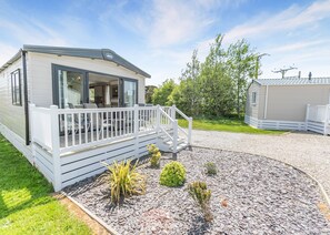 A mobile home with a porch and a small deck, surrounded by gravel and plants.