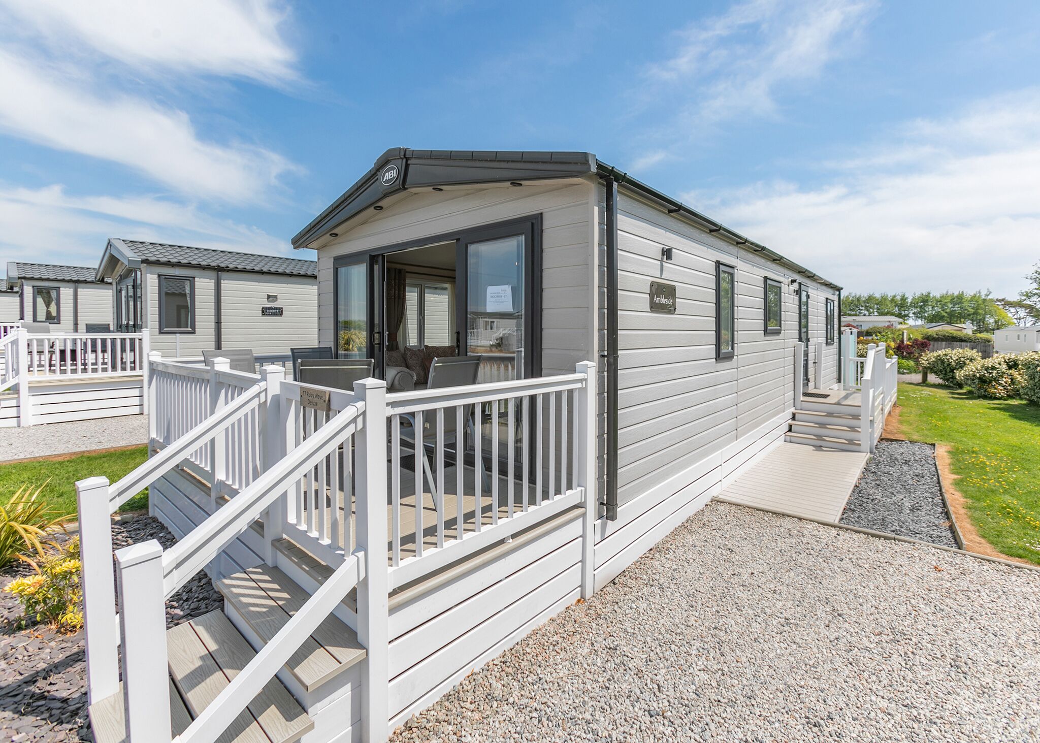 A mobile home with a porch, a small deck, and a gravel driveway.