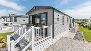 A mobile home with a porch, a small deck, and a gravel driveway.