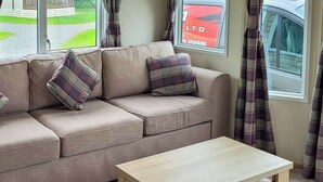 A living room with a beige sofa, two plaid cushions, and a wooden coffee table. - Modern holiday home with a large comfortable living area and dining area. (Arnold)