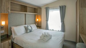 Une chambre d’hôtel avec un lit, des tables de chevet, une fenêtre avec des rideaux et un lambris en bois sur les murs.