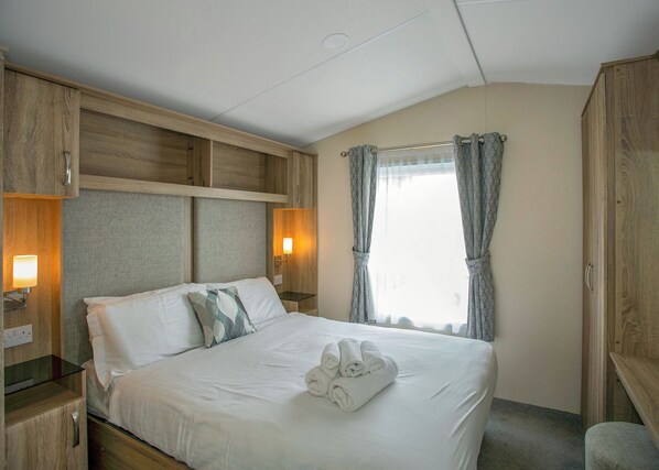 A hotel room with a bed, bedside tables, a window with curtains, and wooden paneling on the walls. - 2 bedroom accommodation in Cowden, Nr Hornsea (Cowden, Nr Hornsea)