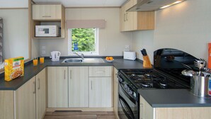 Une cuisine compacte équipée d’un four à micro-ondes, d’un évier, d’une cuisinière et d’une fenêtre donnant sur un paysage verdoyant.