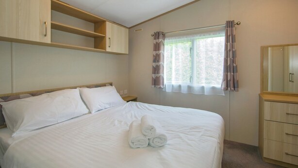 Une chambre à coucher comprenant un lit, une table de chevet, une commode, une fenêtre avec des rideaux et un luminaire au plafond.