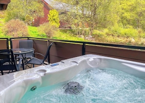 A hot tub with a view of a wooden cabin and greenery.