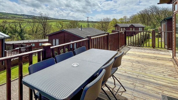 A deck with outdoor seating, a view of the countryside, and a small building with a sloped roof.
