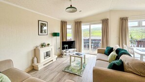 A living room with a fireplace, sofa, TV, and a balcony with outdoor seating.