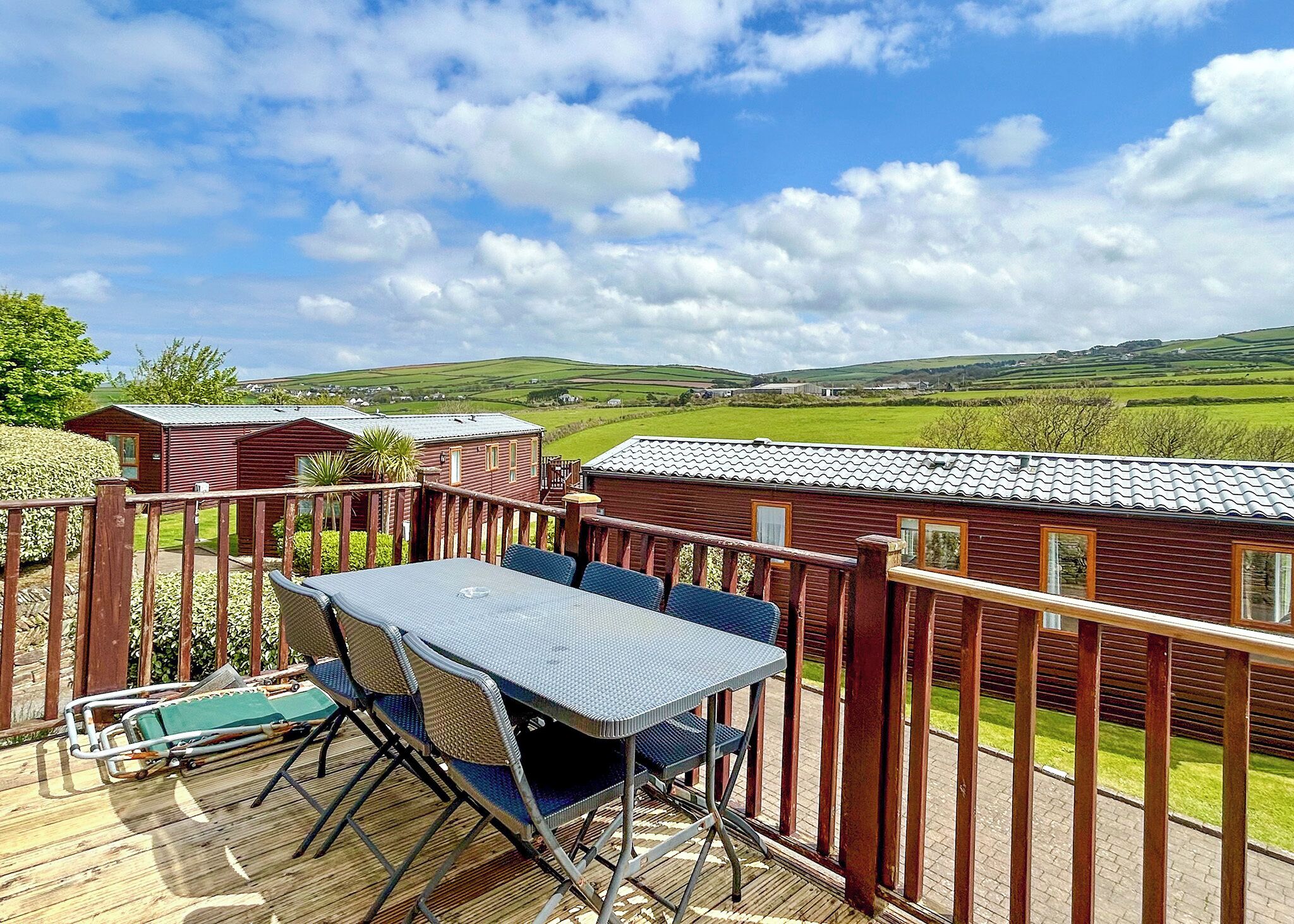 A deck with a table and chairs, overlooking a rural landscape with houses.