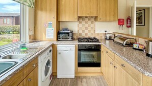 A compact kitchen with wooden cabinets, a washing machine, a microwave, a stove, and a toaster.