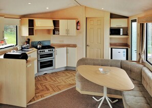 A compact kitchen with a stove, oven, and microwave, a dining area with a table and sofa, and a door leading to another room.