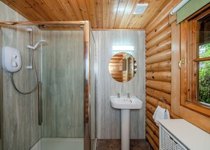 A wooden cabin bathroom with a shower, sink, and mirror. - Timber lodge set in an elevated position with views of the lake. (Webbery, Bideford)