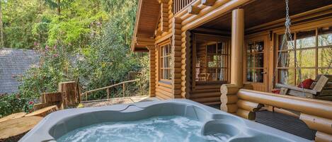 A log cabin with a hot tub and a deck area.