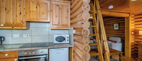 Une cuisine rustique aménagée dans une cabane en rondins, avec des meubles en bois, un four à micro-ondes, un four traditionnel et une échelle.