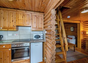 A log cabin kitchen with wooden cabinets, a microwave, an oven, and a ladder.