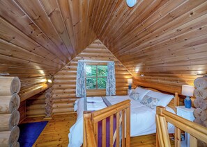 A log cabin bedroom with a bed, a window with curtains, a nightstand, and a lamp. - Timber lodge set in an elevated position with views of the lake. (Webbery, Bideford)