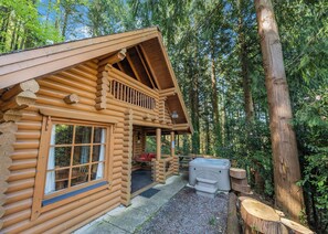 A log cabin with a porch, a hot tub, and a forested backdrop. - Timber lodge set in an elevated position with views of the lake. (Webbery, Bideford)