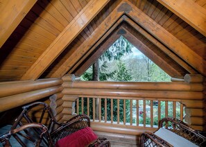 Eine Blockhütte mit Balkon, Holzwerteln und Blick auf Bäume.