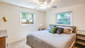 Una camera da letto con un letto, un ventilatore a soffitto, due finestre, un comodino e una lampada.