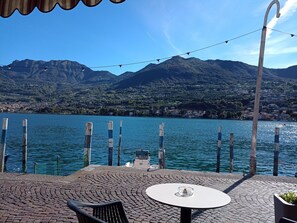 A waterfront patio with a table and chairs, wooden posts, and a view of a lake with mountains in the background.