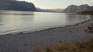 Een kiezelstrand aan een meer, met bergen op de achtergrond.