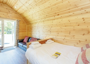 A wooden cabin bedroom with a bed, a bench, and a view of the outdoors. - Comfortable pod perfect for short stays for couples with a sense of fun. (Hawes,)