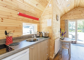 A wooden cabin interior with a kitchen, a dining area, and a window with a view. - Comfortable pod perfect for short stays for couples with a sense of fun. (Hawes,)