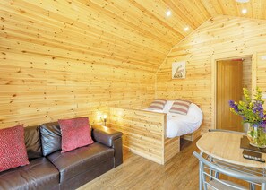 A wooden cabin interior with a bed, a sofa, a table, and a vase with flowers. - Comfortable pod perfect for short stays for couples with a sense of fun. (Hawes,)