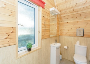 A wooden-paneled bathroom with a window, sink, toilet, and a small potted plant. - Comfortable pod perfect for short stays for couples with a sense of fun. (Hawes,)